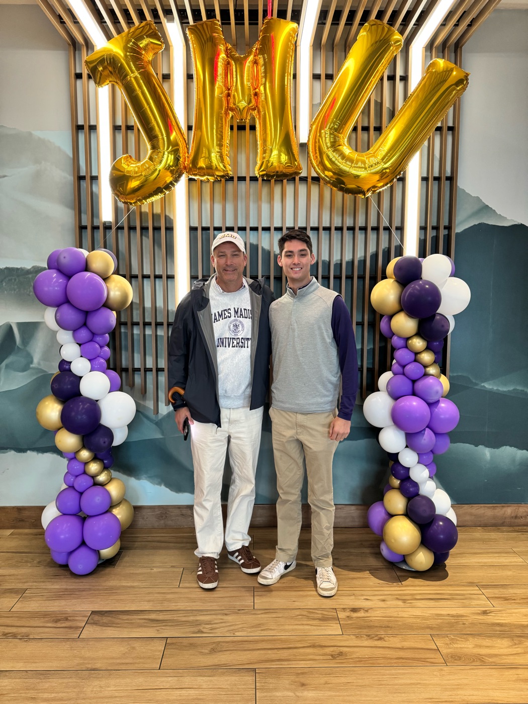 Kevin and an older man in a JMU shirt standing under gold JMU balloons
