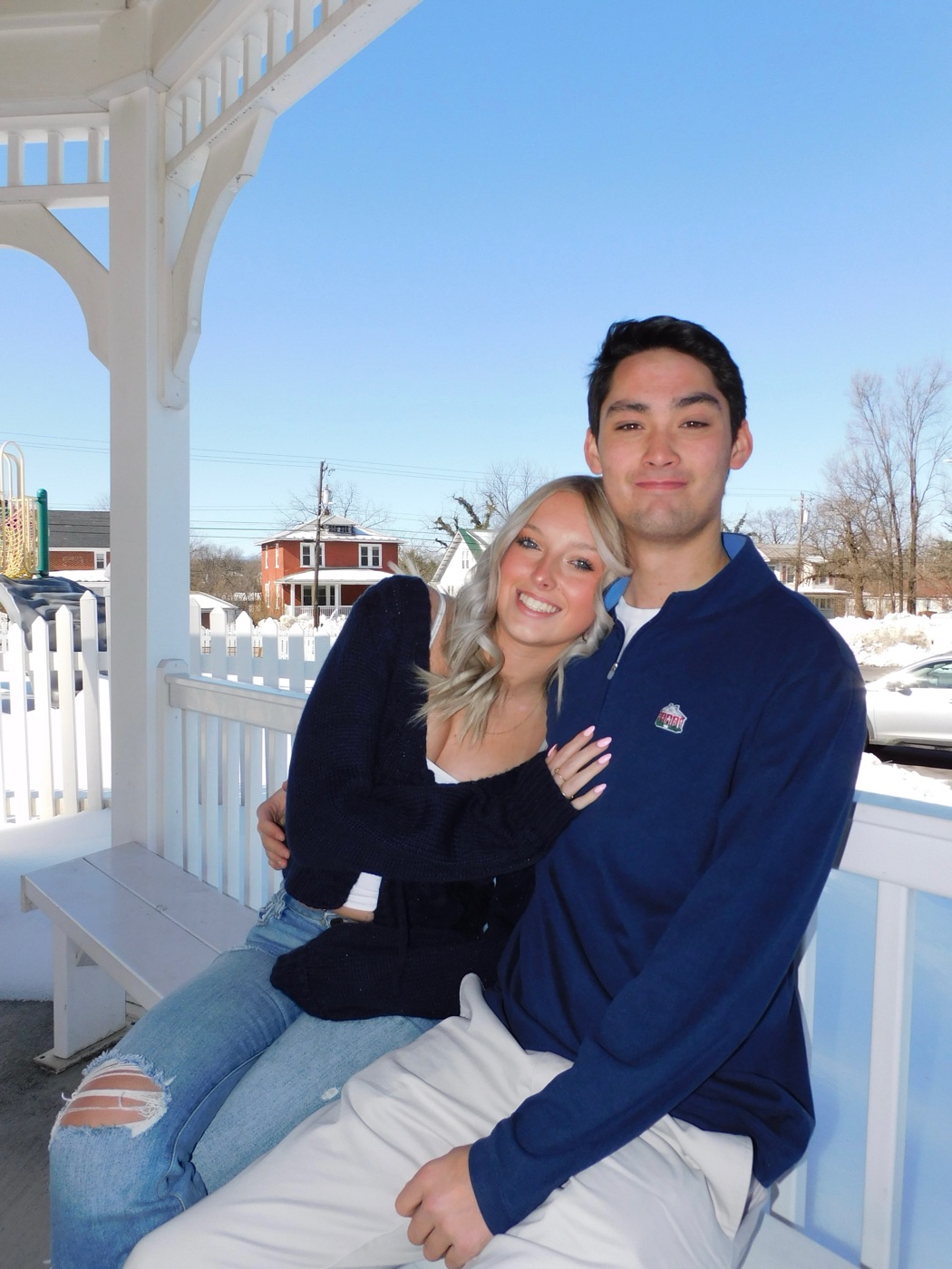 Kevin and his girlfriend sitting together on a white porch bench on a sunny winter day